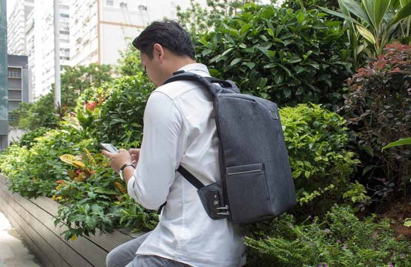 Man on iPhone Sitting in Garden with Back Pack